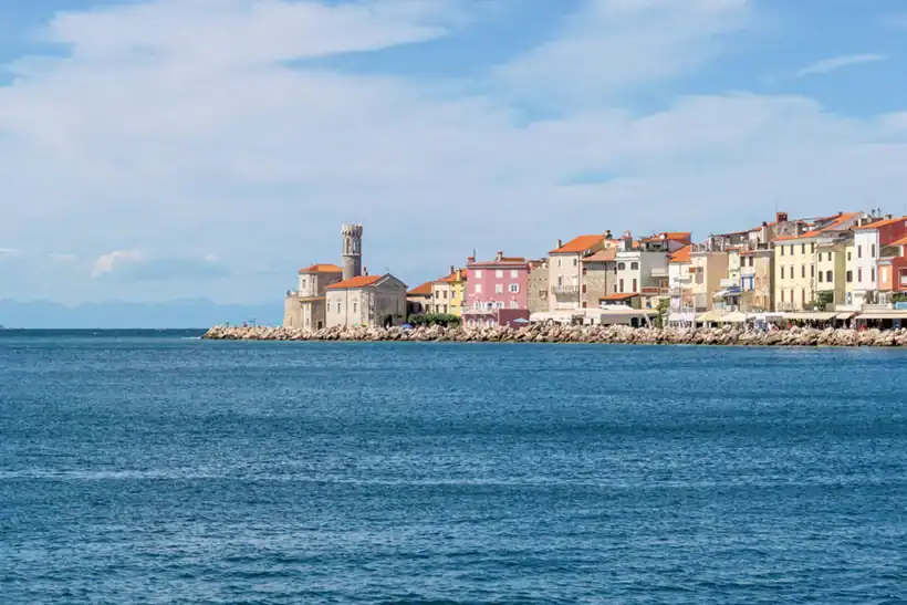 Sončen pogled na Piran z modrim nebom in obalo, značilno za Primorsko.