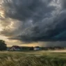 Temen nevihtni oblak nad slovensko podeželsko pokrajino z nalivom v ozadju in vetrom pred prihajajočo poletno nevihto.